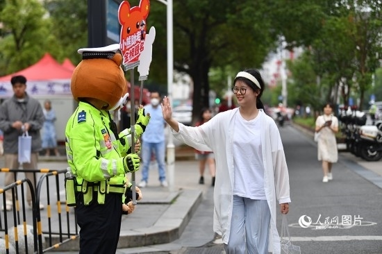 6月7日上午9時，隨著鈴聲的響起，2023年江西高考正式開考，江西省的53.57萬考生以縣（區(qū)）為單位隨機安排在全省256個考點、18968個考場參加高考。圖為“小熊交警”和考生擊掌鼓勵。 人民網(wǎng)記者 時雨攝