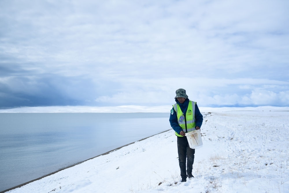 2021年10月20日，在青海省果洛藏族自治州瑪多縣扎陵湖鄉(xiāng)勒那村，三江源國家公園黃河源園區(qū)生態(tài)管護(hù)員在扎陵湖邊撿拾垃圾。新華社記者 張龍 攝