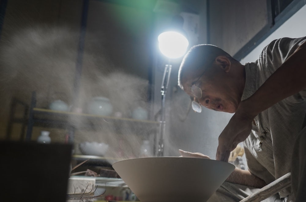 ↑ 在景德鎮(zhèn)，手工匠人吹去坯內(nèi)的泥土（2021年7月14日攝）。