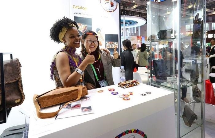 11月6日，一位參觀者（右）在第六屆進(jìn)博會國家展南非展臺試戴傳統(tǒng)首飾。