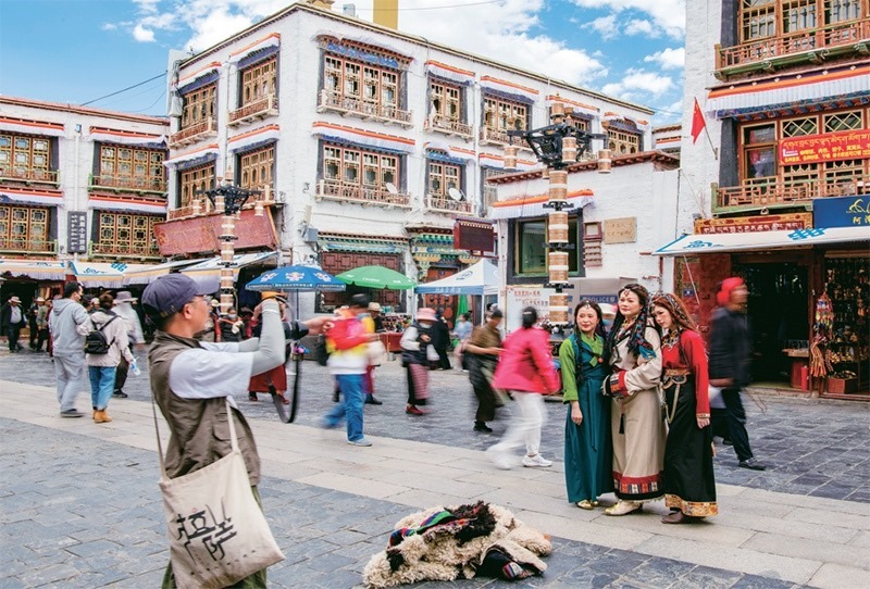 千年八廓街，見證民族團(tuán)結(jié)。2021年7月，習(xí)近平總書記來到位于西藏拉薩老城區(qū)的八廓街，感慨地說：“千年八廓街，是我們各民族建起來的八廓街。各民族文化在這里交流交往交融，我們中華民族的大家庭在這里其樂融融?！眻D為2023年6月13日，游客身著藏裝在八廓街拍照留念。 新華社記者 姜帆/攝