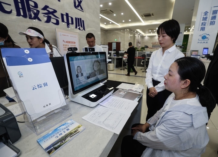 在浙江省嘉興市秀洲區(qū)王江涇鎮(zhèn)便民服務(wù)中心的“跨域通辦·云綜窗”窗口，辦理開(kāi)業(yè)登記的個(gè)體工商戶(hù)（右一）通過(guò)該系統(tǒng)與江蘇省蘇州市吳江區(qū)盛澤鎮(zhèn)行政審批局工作人員視頻連線(xiàn)，進(jìn)行身份讀取及材料線(xiàn)上審核（2024年5月9日攝）。新華社記者 徐昱 攝