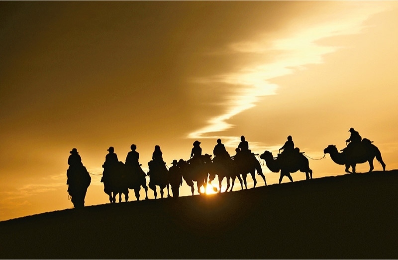 新時(shí)代以來(lái)，文化和旅游深度融合發(fā)展體制機(jī)制不斷健全，成功走出了一條獨(dú)具特色的中國(guó)旅游發(fā)展之路。圖為2024年9月1日清晨，游客在甘肅省敦煌市鳴沙山月牙泉景區(qū)乘騎駱駝，欣賞大漠風(fēng)光，體驗(yàn)絲路風(fēng)情。 新華社發(fā) 張曉亮/攝