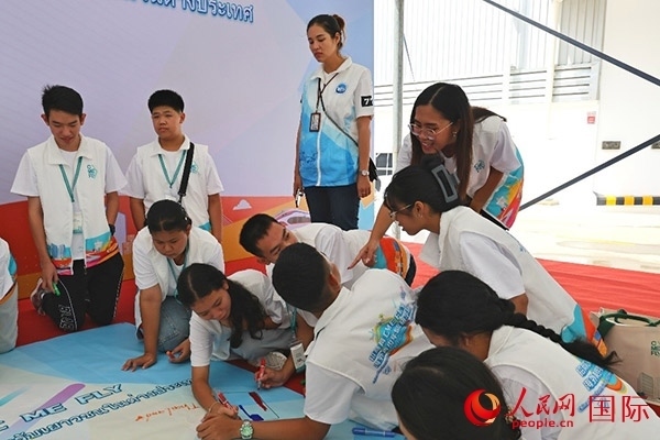 泰國學(xué)生在開營儀式展板上繪制圖案。人民網(wǎng)記者 白元琪攝